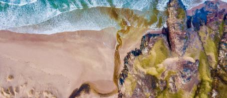An aerial photograph of a sea shore with sand and rocks